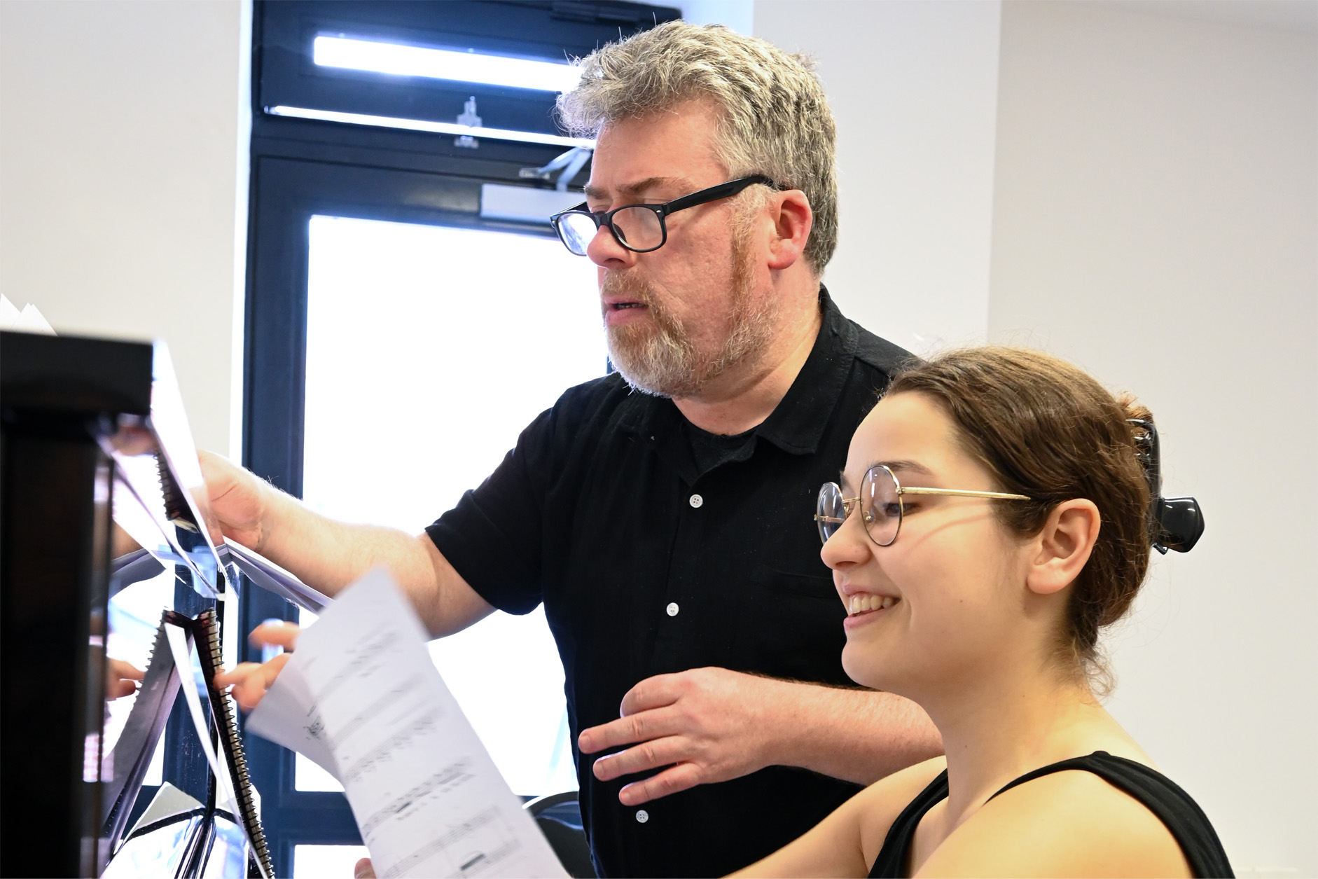 A male professor and a female student looking and writing on music sheets on a piano.